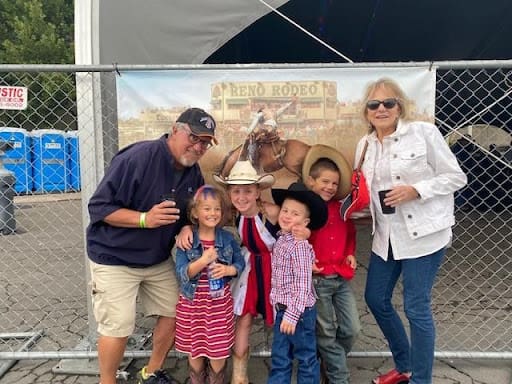 A group of two adults and four kids standing against a chain link fence.