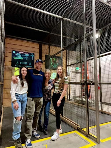 Four people standing in an axe throwing cage.