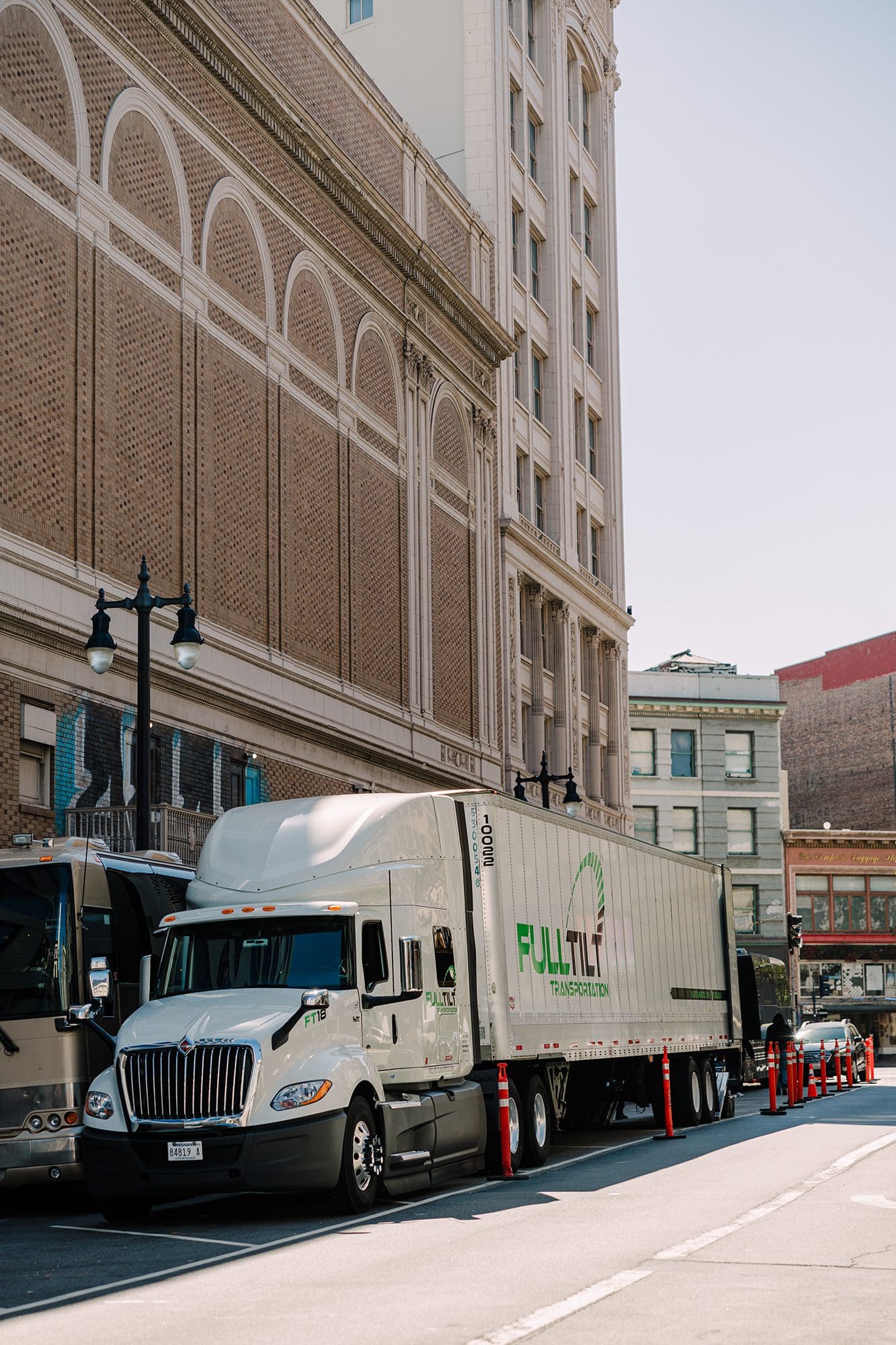 A Full Tilt Logistics truck is parked next to a tour bus