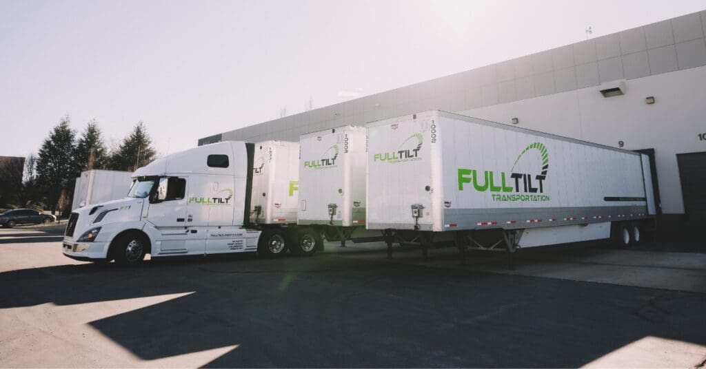 A Full Tilt truck is parked next to 2 Full Tilt trailers at a dock